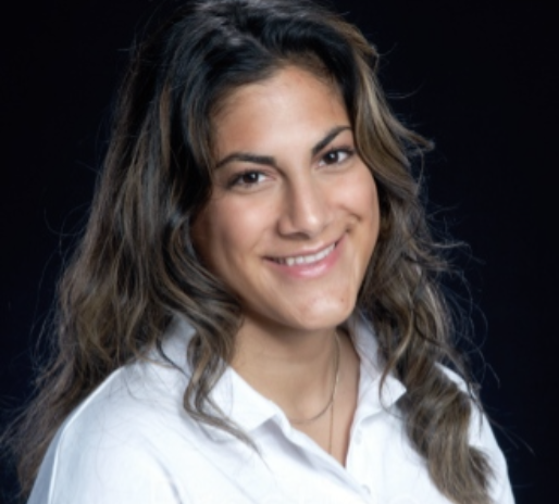 Headshot of Nadia Bhatti smiling in a white shirt against a black background