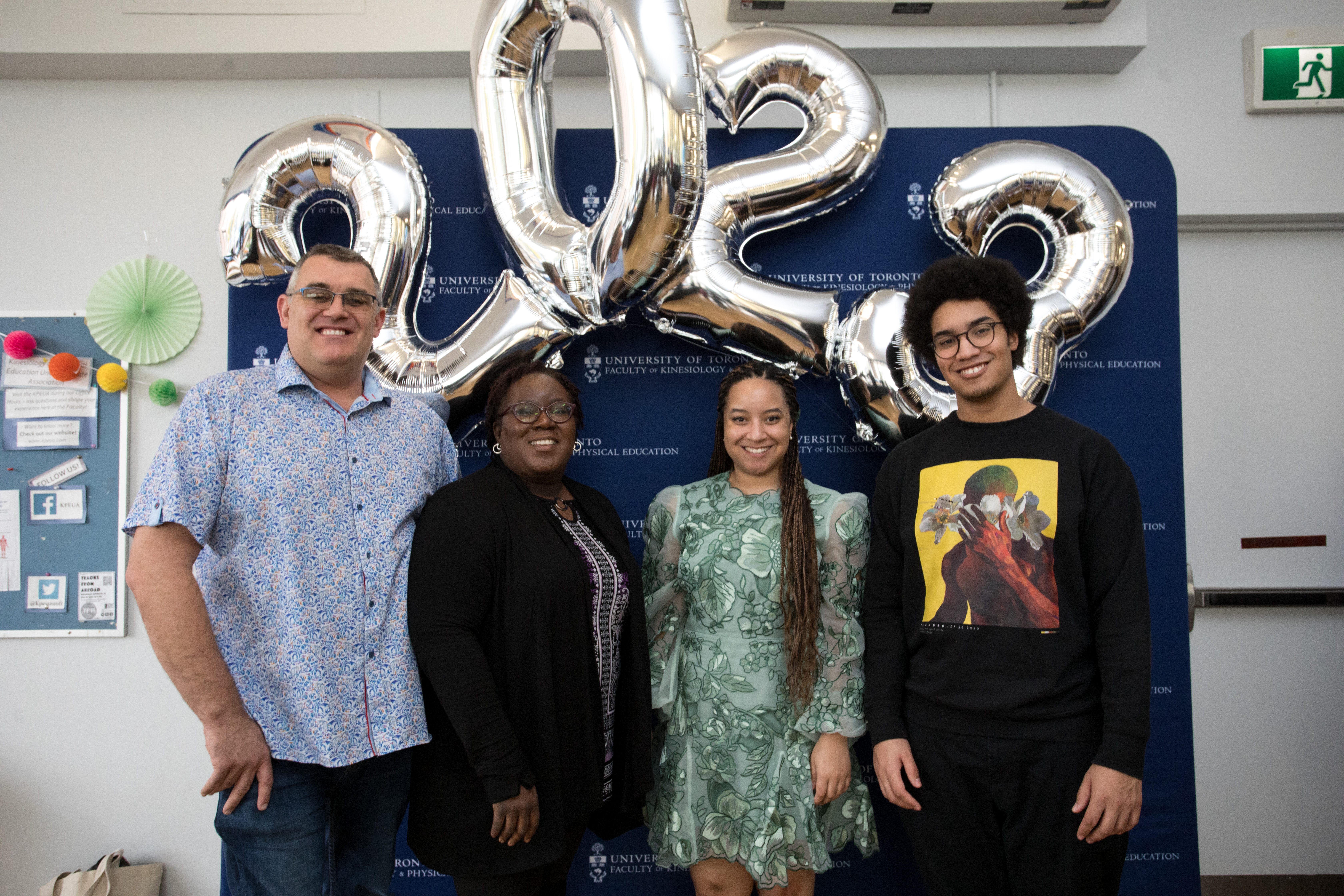 Shalom Brown with family in front of faculty backdrop and balloons