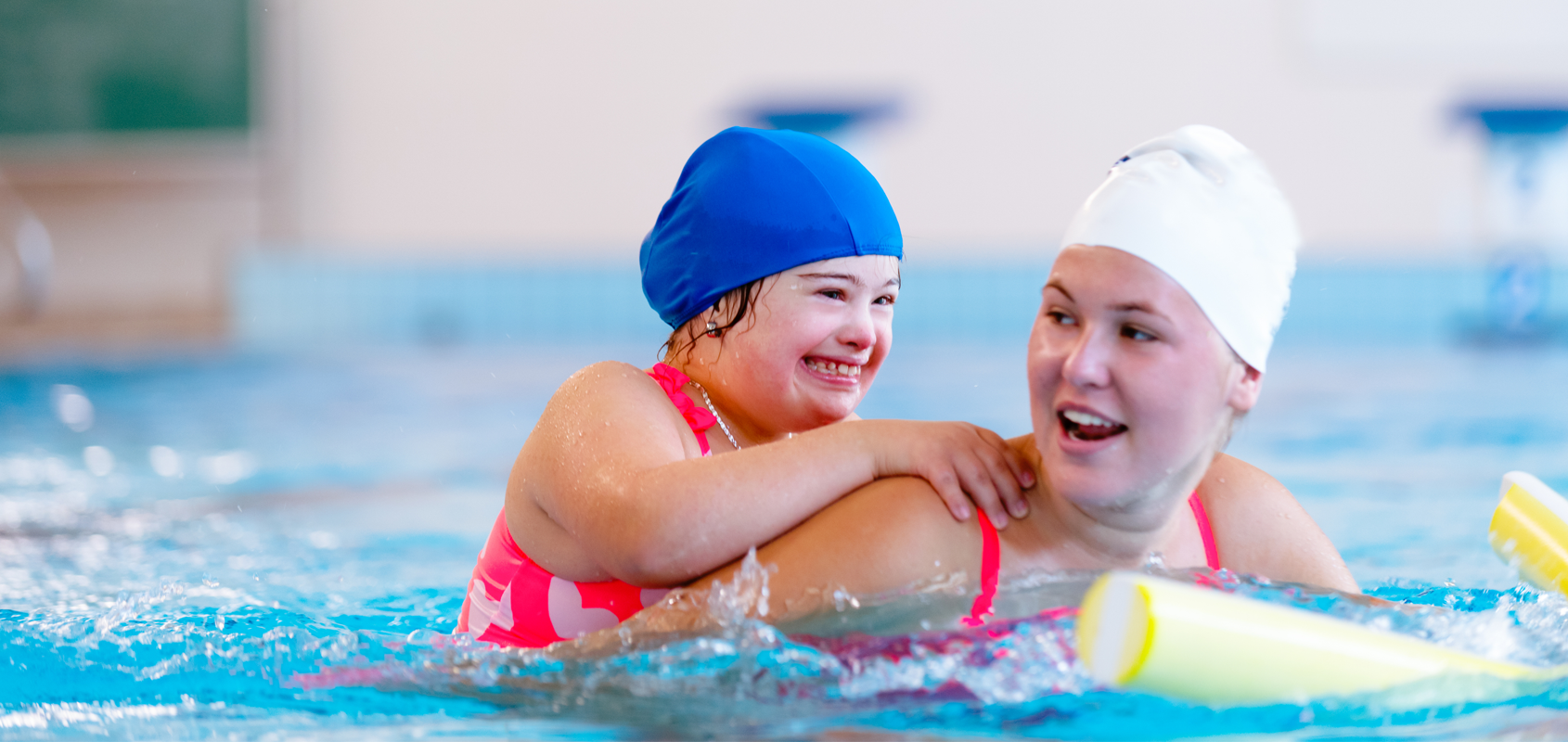 instructor helps child with down syndrome in swimming pool