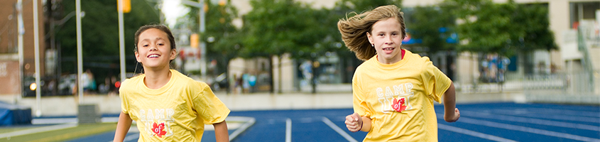 Two girls wearing yellow t-shirts running towards the camera on the track